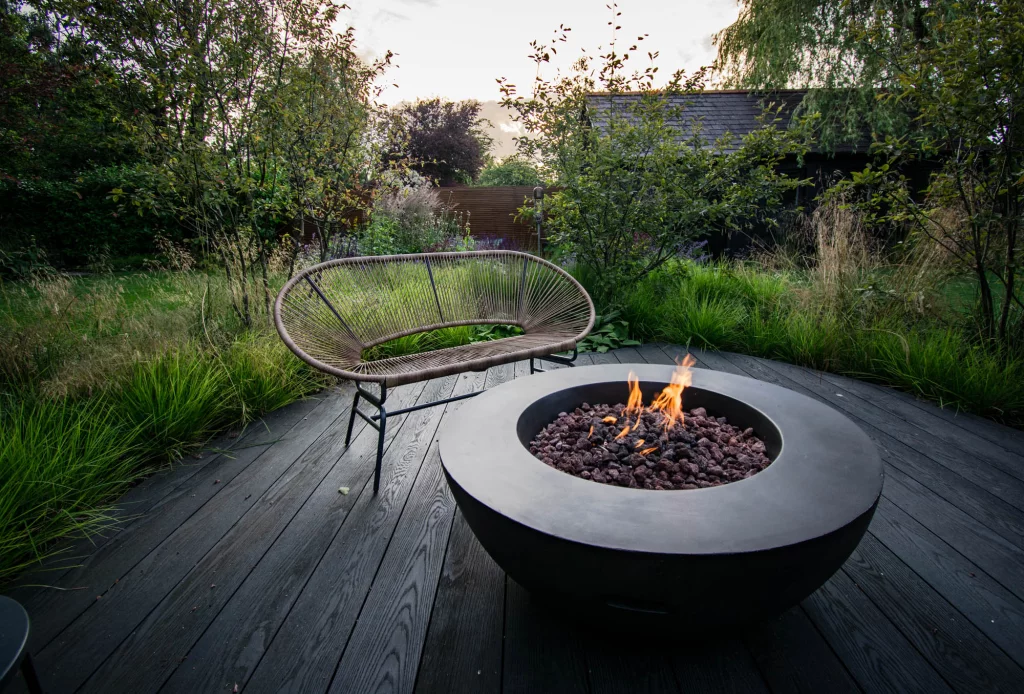 Contemporary fire bowl on dark timber decking at dusk.
