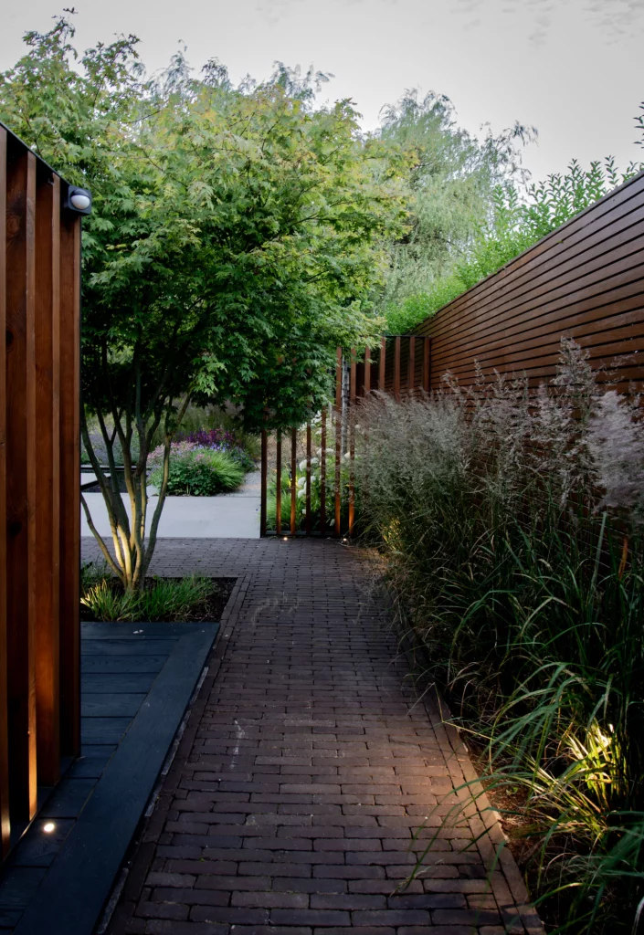 Brick pathway framed by soft grasses and warm wooden fencing.