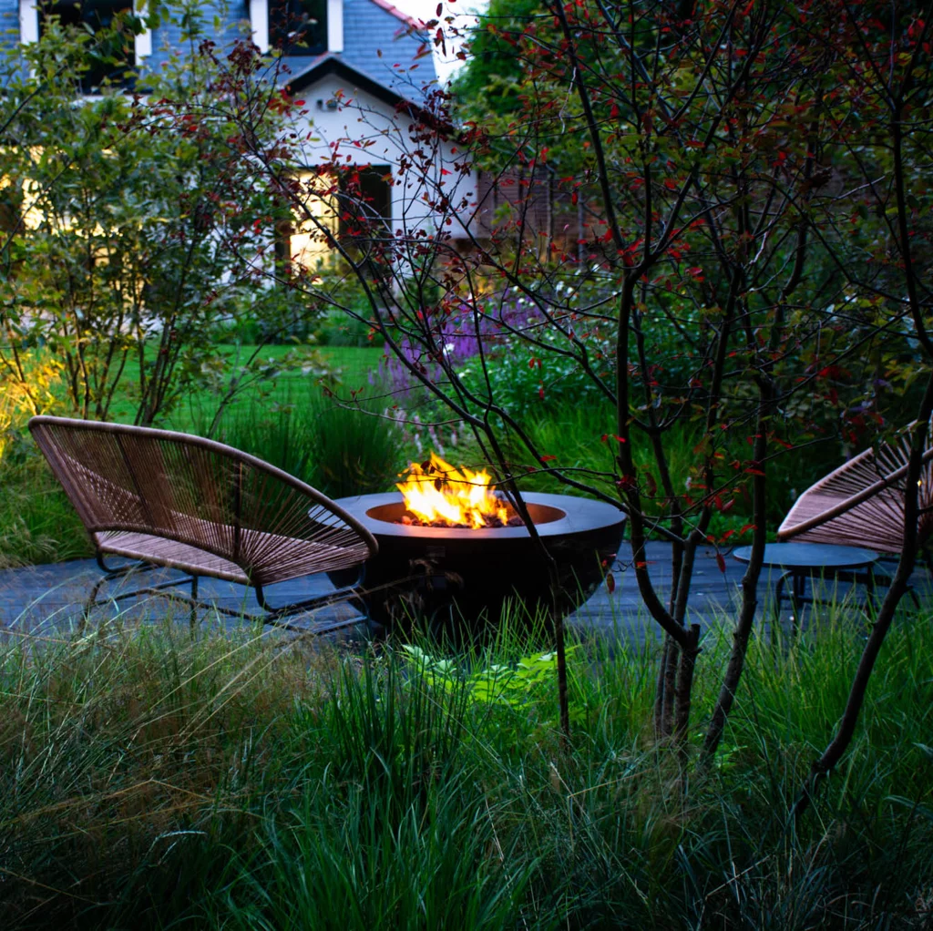 Garden firepit glowing at dusk among soft planting.