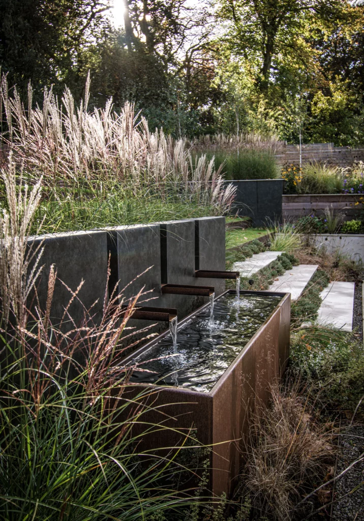 Garden water feature with layered planting and raised corten steel trough.