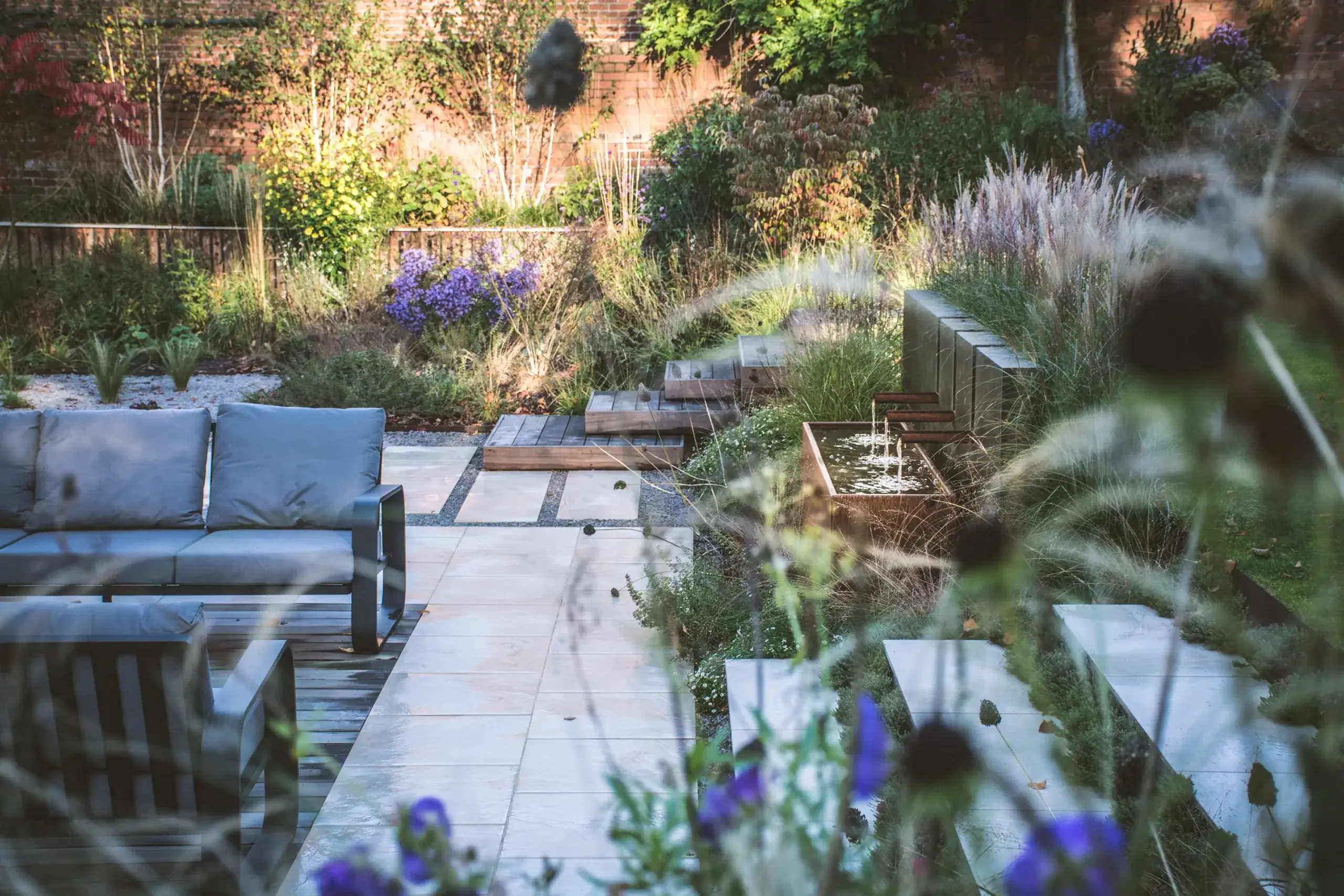 Garden with outdoor seating, water feature, layered planting and stone paths.