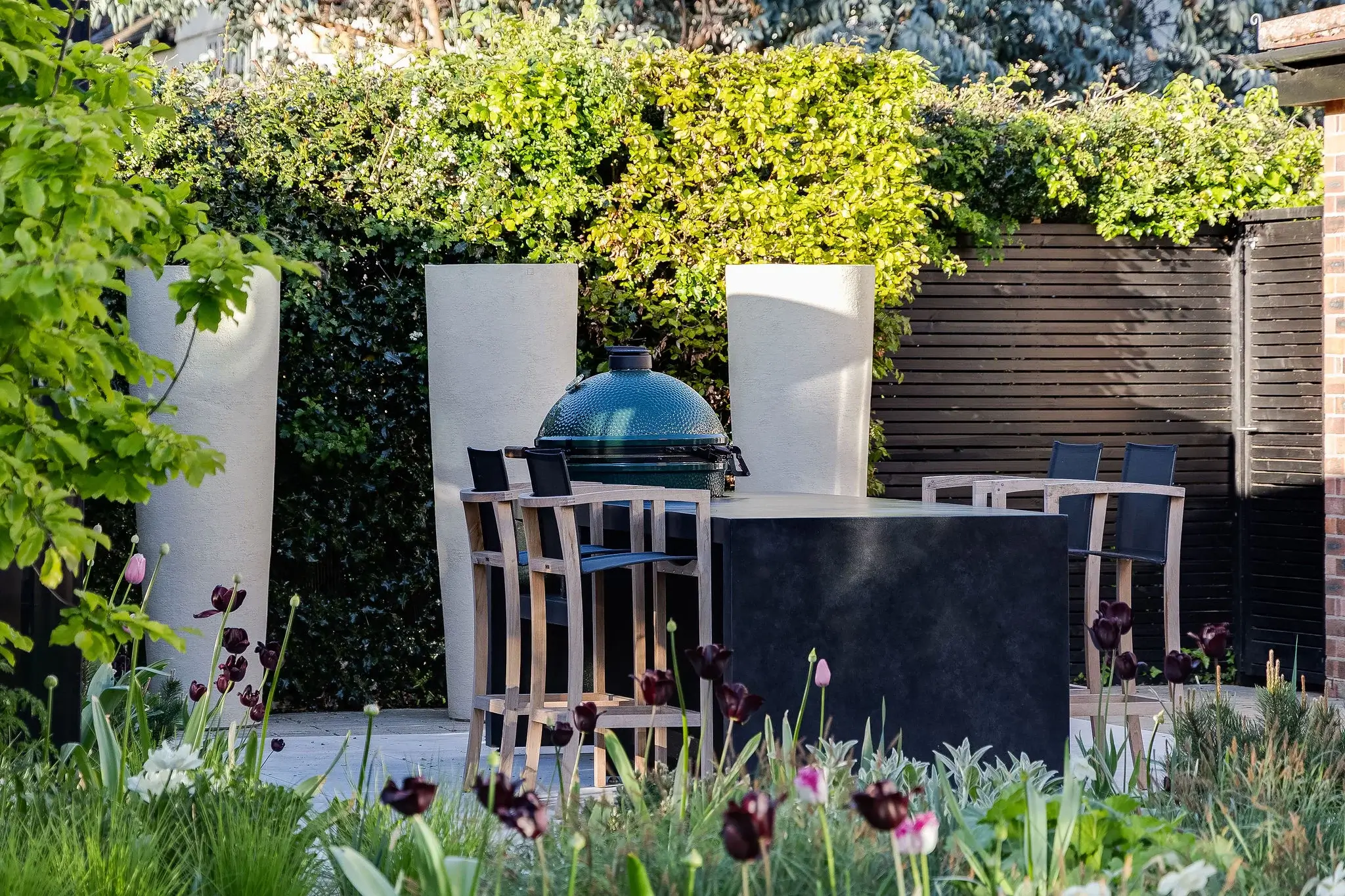 Outdoor kitchen area with a ceramic barbecue and tall planters.
