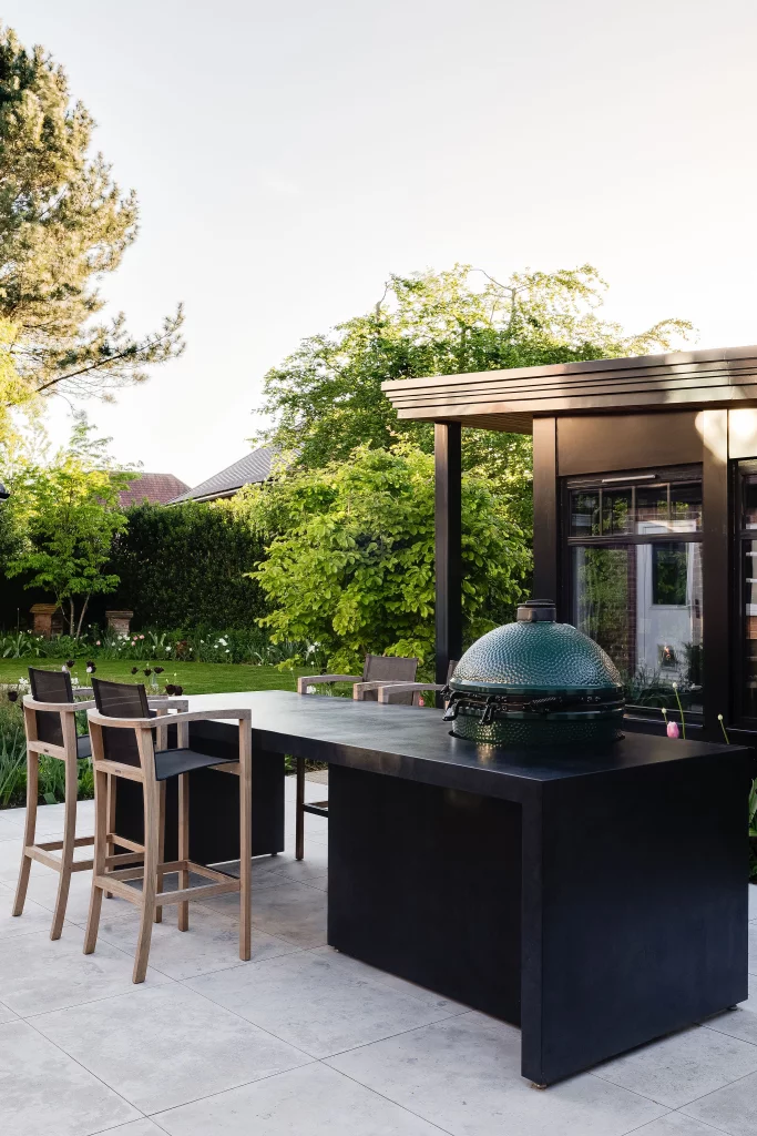 Outdoor dining space with bar seating and ceramic barbecue in garden.