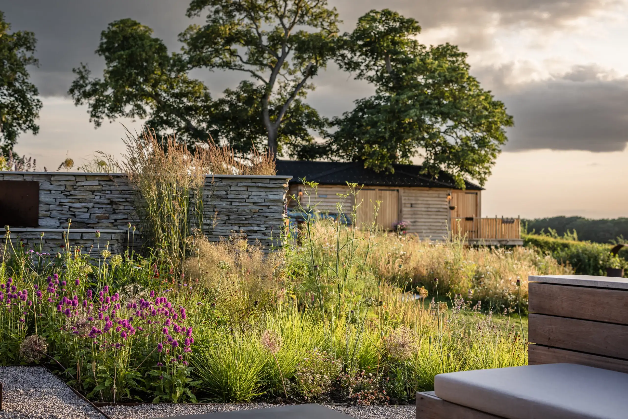 Layered perennial planting against dry-stone walls and open rural views.