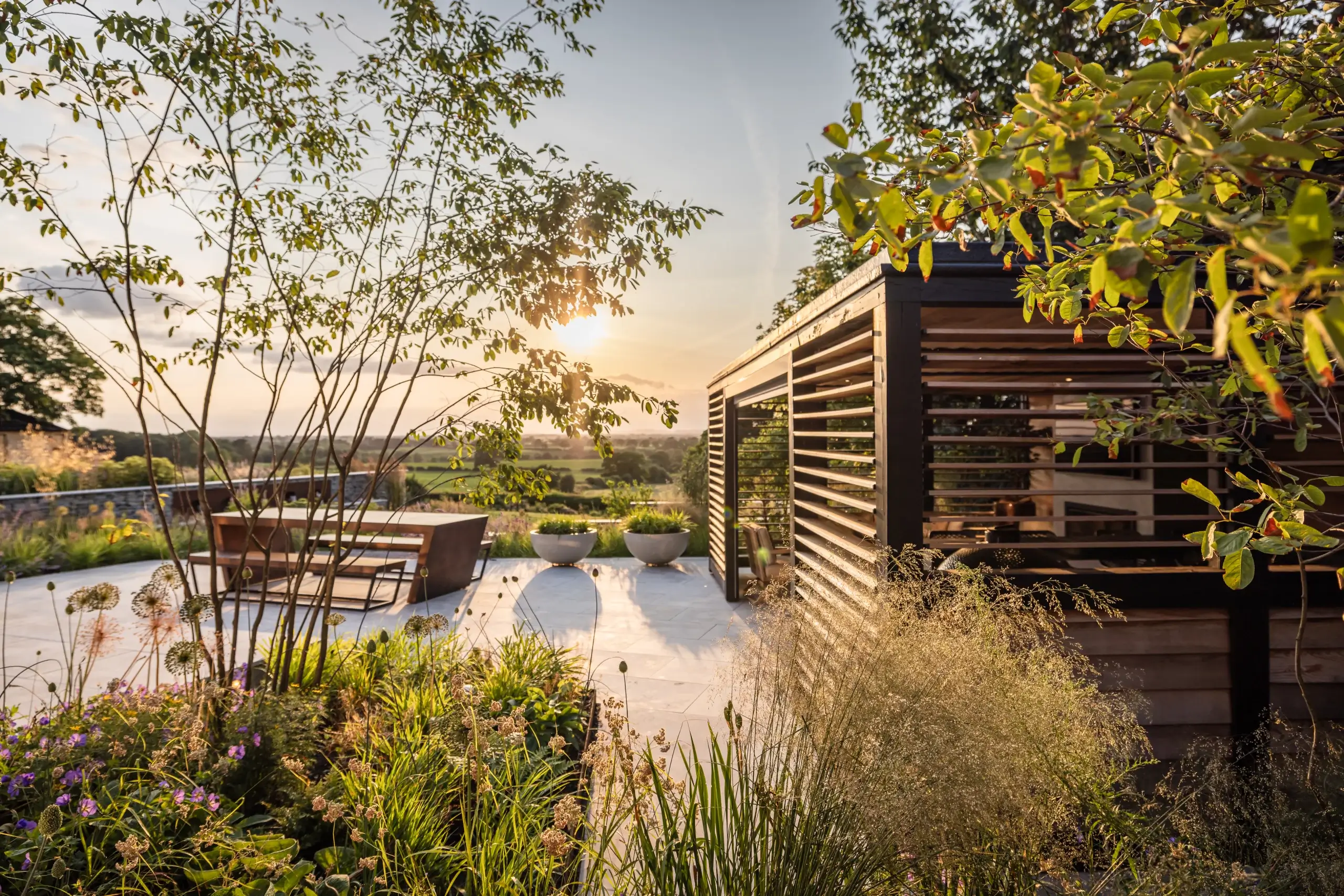 A contemporary garden with a paved terrace, planting beds and a timber pergola.