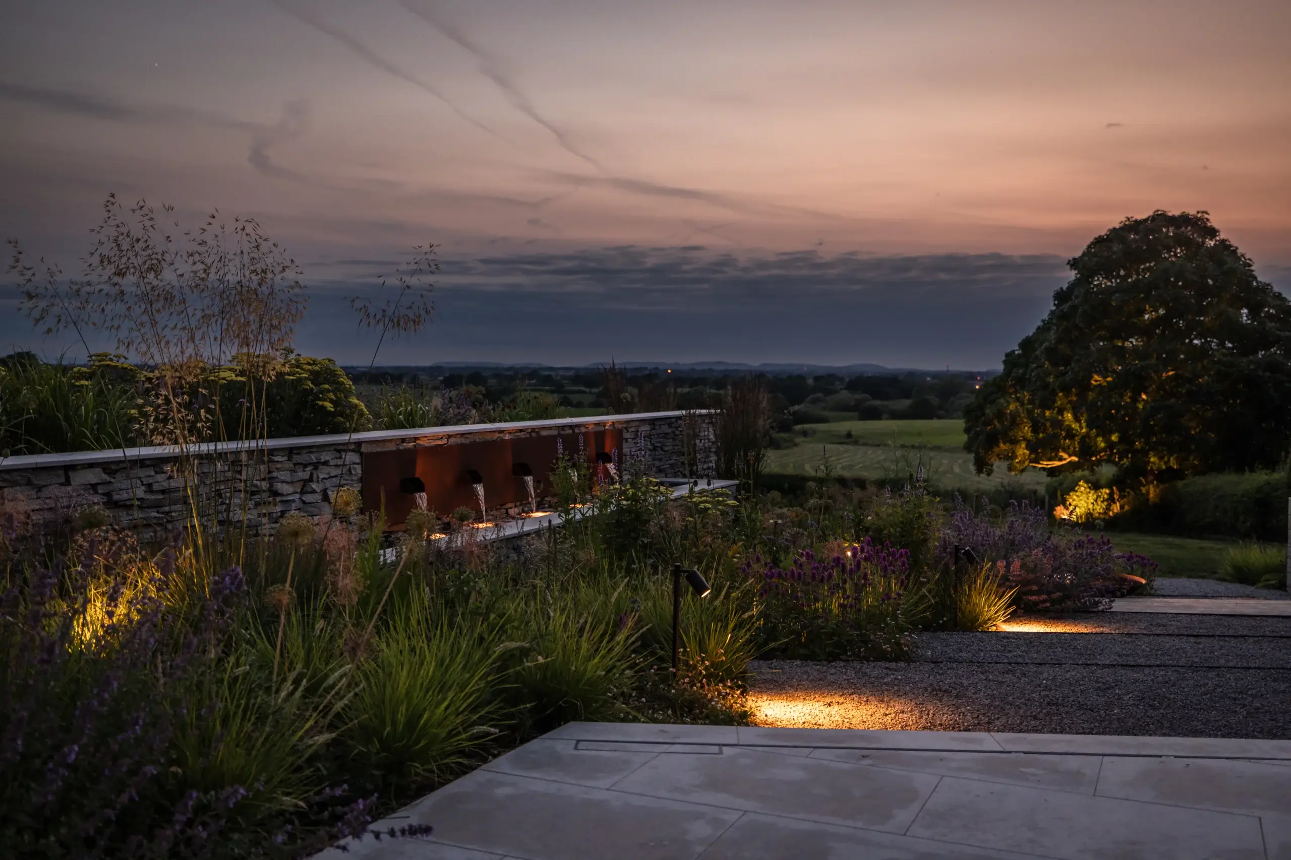Layered garden planting with stone wall and subtle evening lighting.