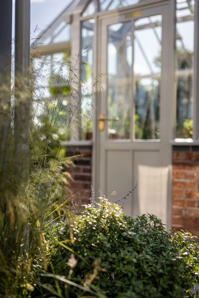 Ornamental grasses and soft planting near a greenhouse doorway.