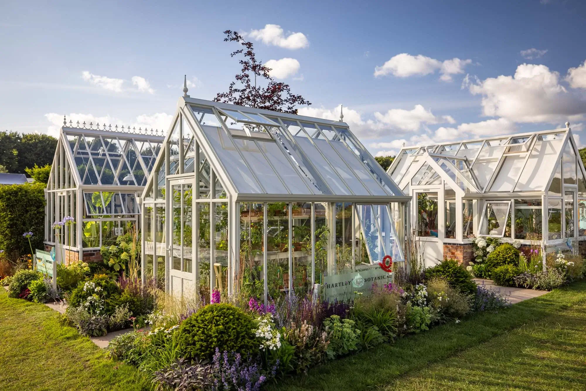 Elegant white greenhouses surrounded by lush planting and summer flowers.