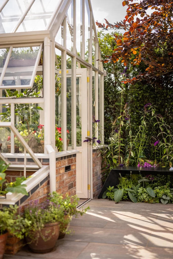 Elegant greenhouse entrance framed by soft planting and terracotta pots.