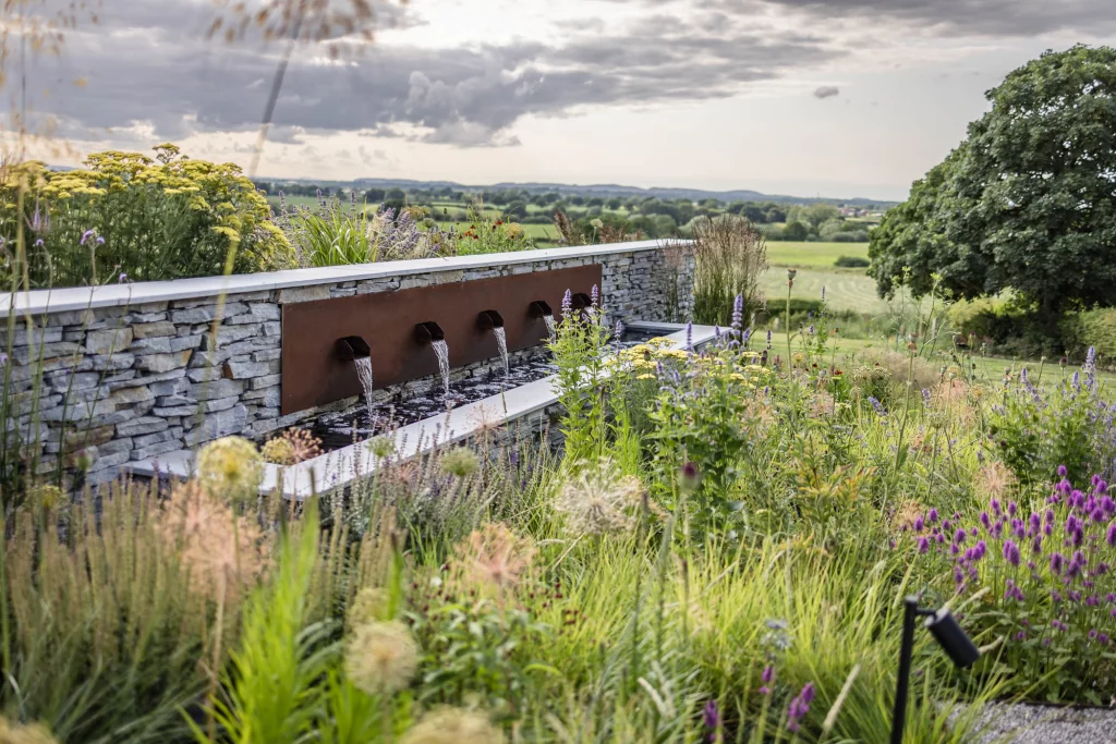 Stone water feature surrounded by layered planting and countryside views.