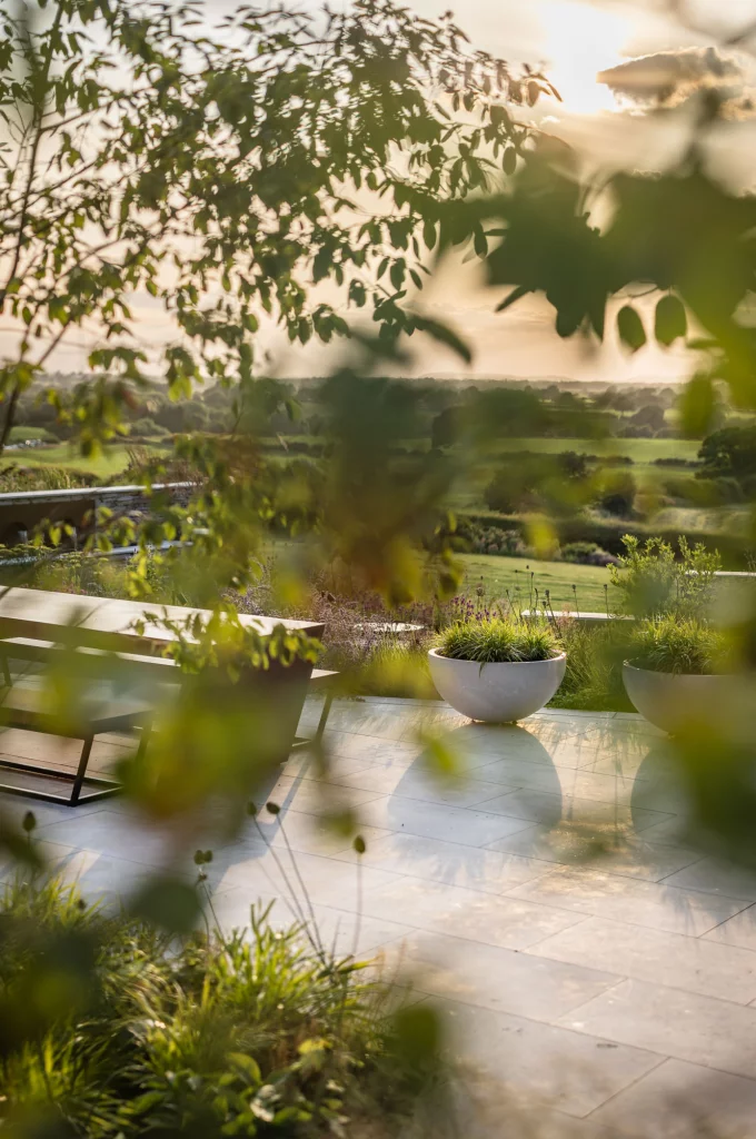 Contemporary garden terrace glimpsed through planting, with distant rural views.
