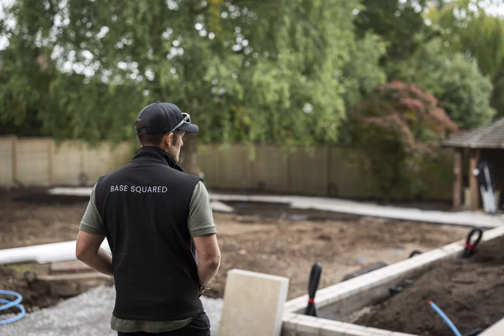 Base Squared team member overseeing groundwork preparations on site, wearing branded vest and cap.