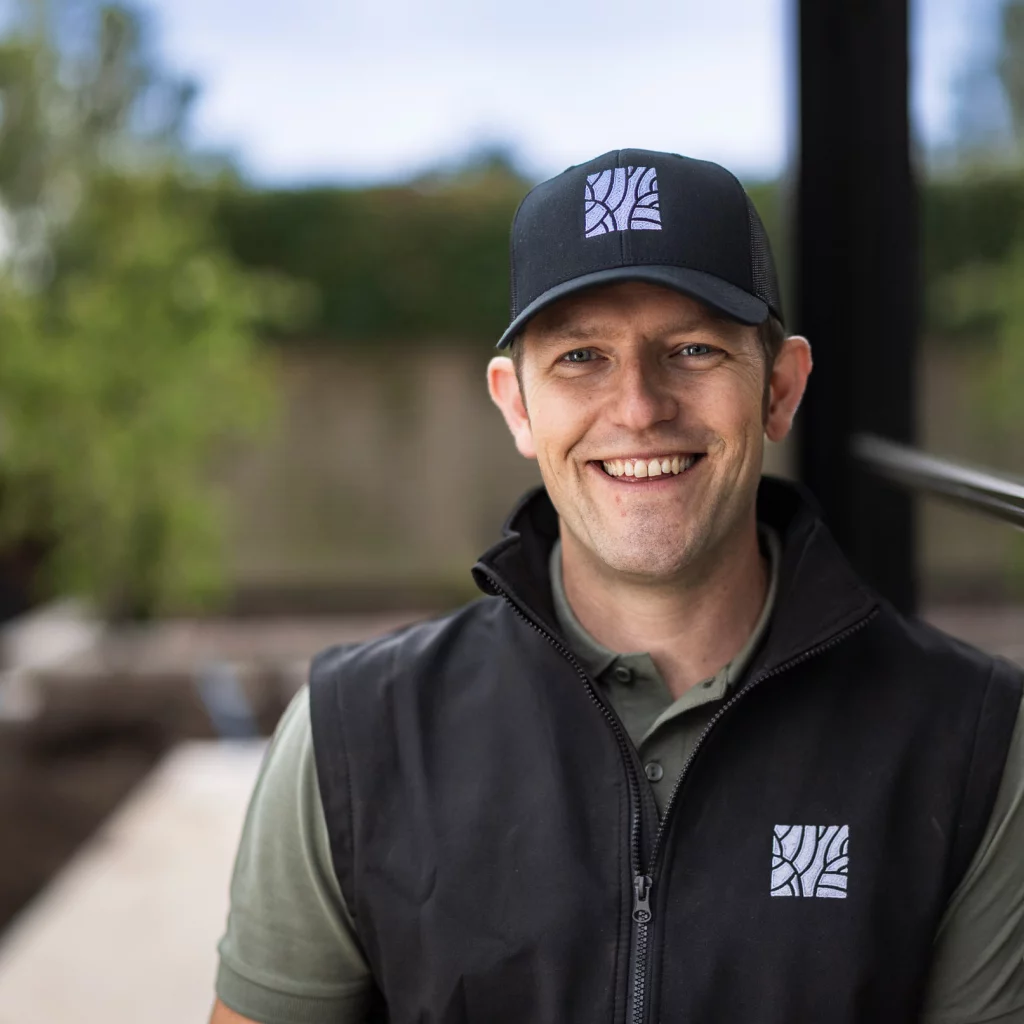 Tom Hearn, smiling in a black branded gilet and cap.